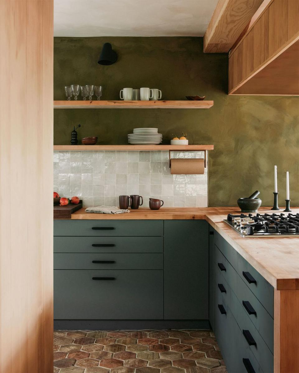 a kitchen terra cotta tiles on the floor and green cabinets and woodwork with a stove and shelves and a small area of white tile backsplash