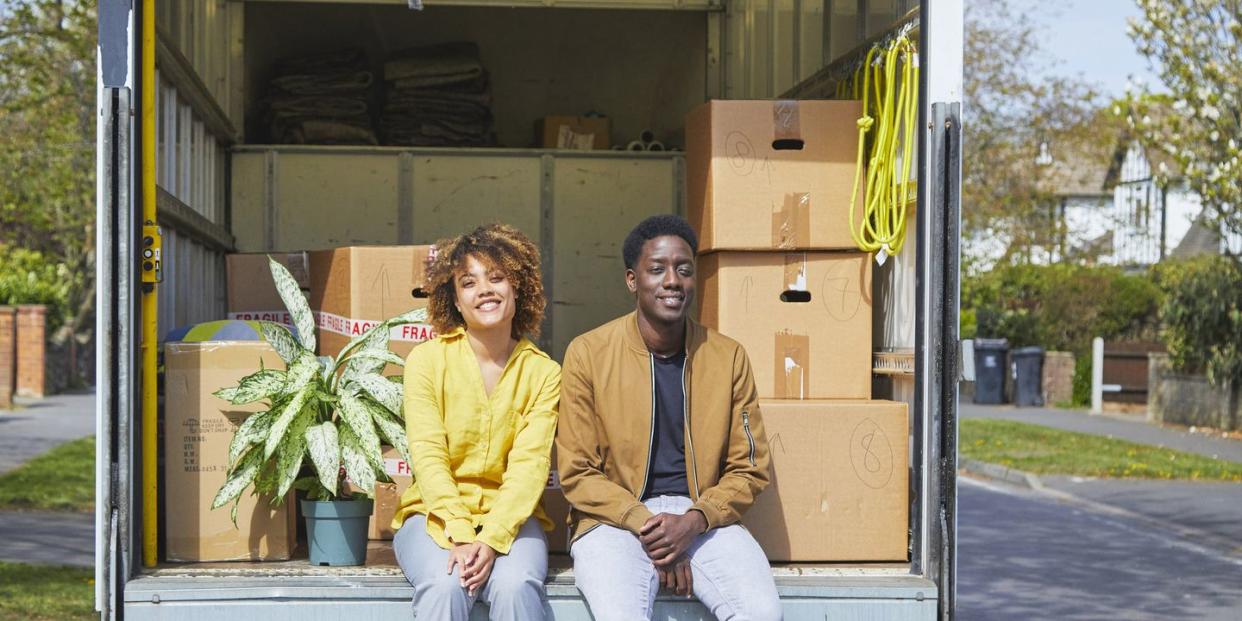 young couple moving house they are sitting in back of the removal van amongst boxes