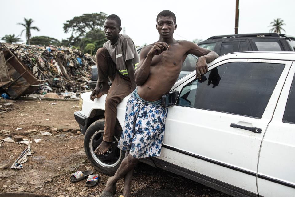 Two men relax on a car at the Kington landfill site in Freetown on June 21, 2023. In recent years Kush, a mix of various chemicals and plants that mimic the natural properties found in cannabis, according to the National Drug Agency, is increasingly being used by youth in Sierra Leone.