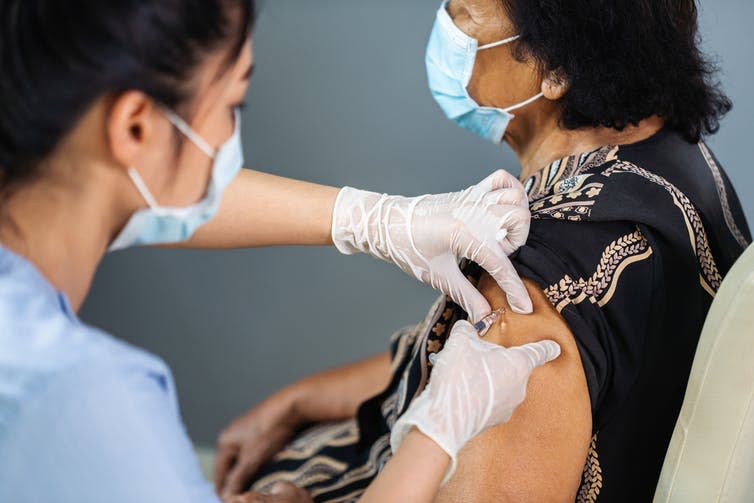 Woman doctor giving older Indian woman a vaccine shot into the shoulder