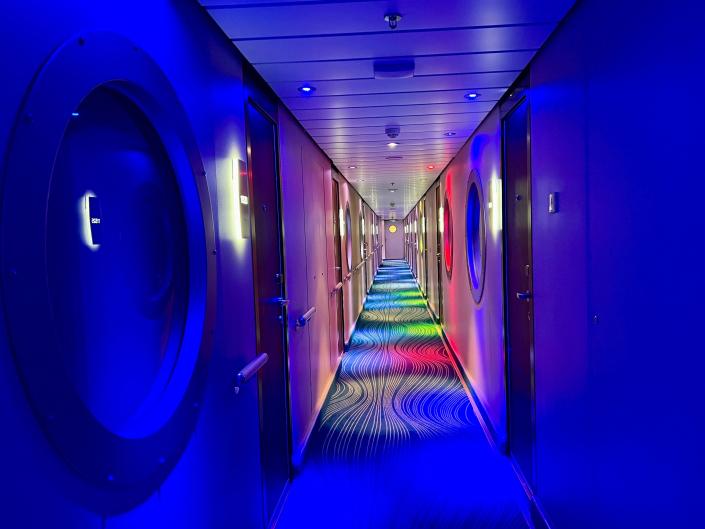 Norwegian Getaway hallway with studio staterooms - lit up in blue, orange, and yellow