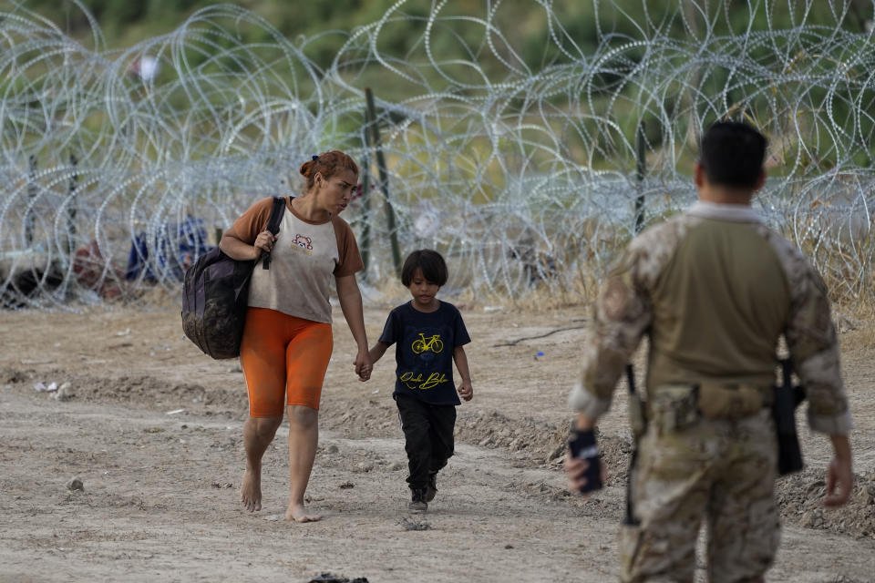Migrants who crossed into the U.S. from Mexico walk past concertina wire lining the banks of the Rio Grande as they move to an area for processing, Sept. 21, 2023, in Eagle Pass, Texas. Migrants have always come to the U.S., but the immigration system now seems strained nationwide more than ever. (AP Photo/Eric Gay)