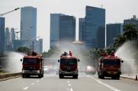 Firefighters spray disinfectant using high pressure pump trucks to prevent the spread of coronavirus disease (COVID-19), on the main road in Jakarta