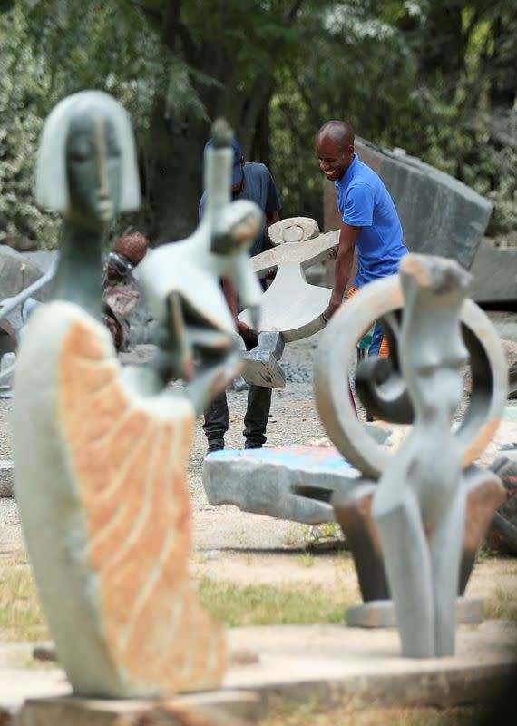 Zimbabwean sculptor Dominic Benhura carries a finished piece at his studio in Harare