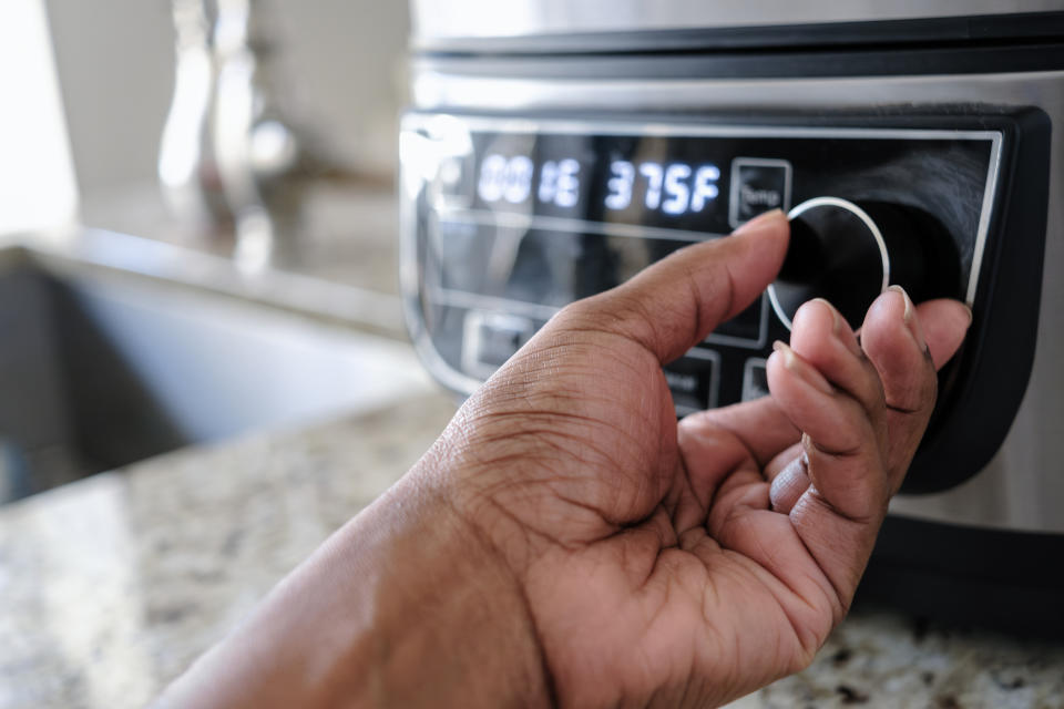 Close-up of a person adjusting an oven temperature to 375 degrees Fahrenheit, focusing on the hand and dial