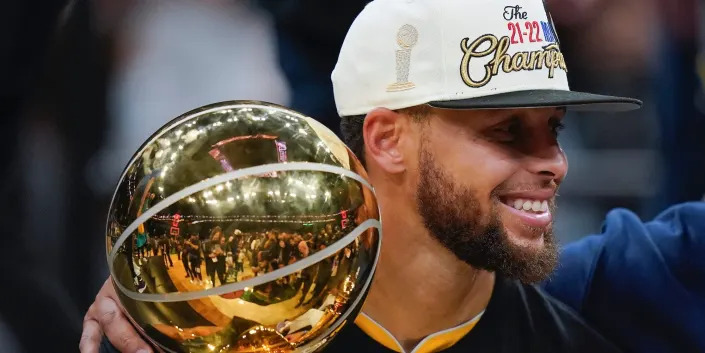Stephen Curry smiles while holding the Larry O'Brien Trophy.