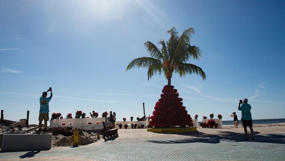 Visitors to Times Square on Fort Myers Beach get photos of the Poinsettia tree that was put up by the Town of Fort Myers Beach on Thursday, Dec. 1, 2022. The area was decimated by Hurricane Ian so it was unknown if the tree would tree would go back up. One flower was placed at the site near Thanksgiving which in turn prompted members of the community to place more flowers at the site. Once the tree was built, the remaining flowers were placed on surrounding traffic barriers.  