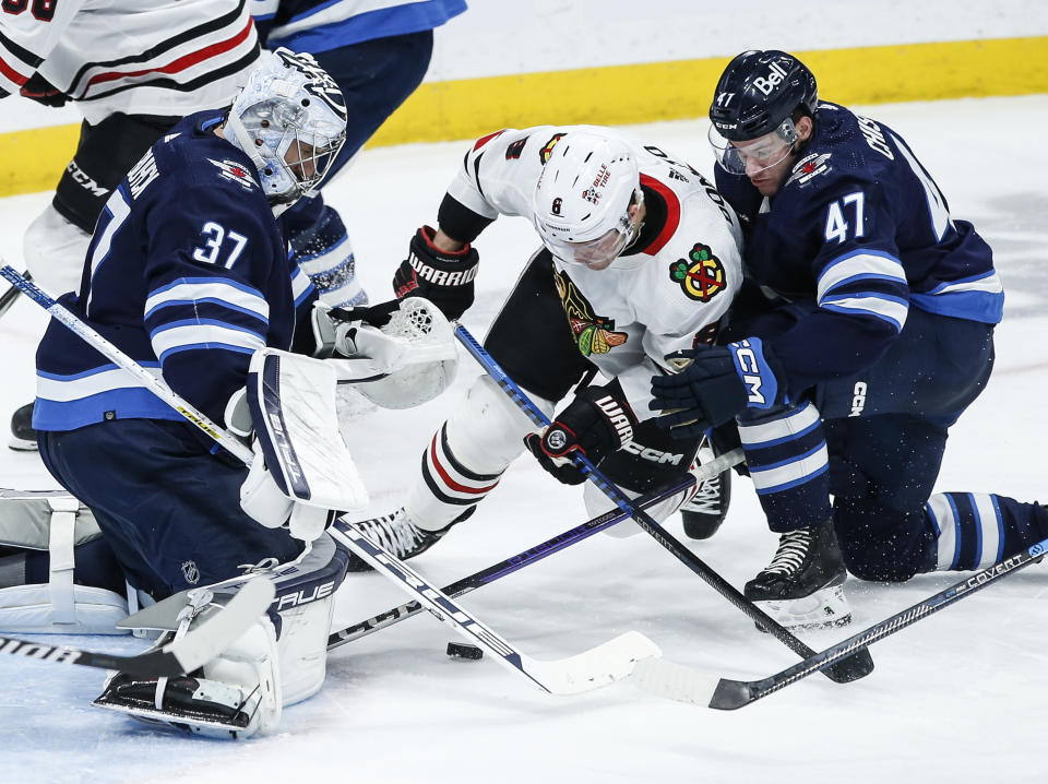 Winnipeg Jets goaltender Connor Hellebuyck (37) saves the shot from Chicago Blackhawks' Ryan Donato (8) as Declan Chisholm (47) defends during the second period of an NHL game in Winnipeg, Manitoba, Saturday, Dec. 2, 2023. (John Woods/The Canadian Press via AP)