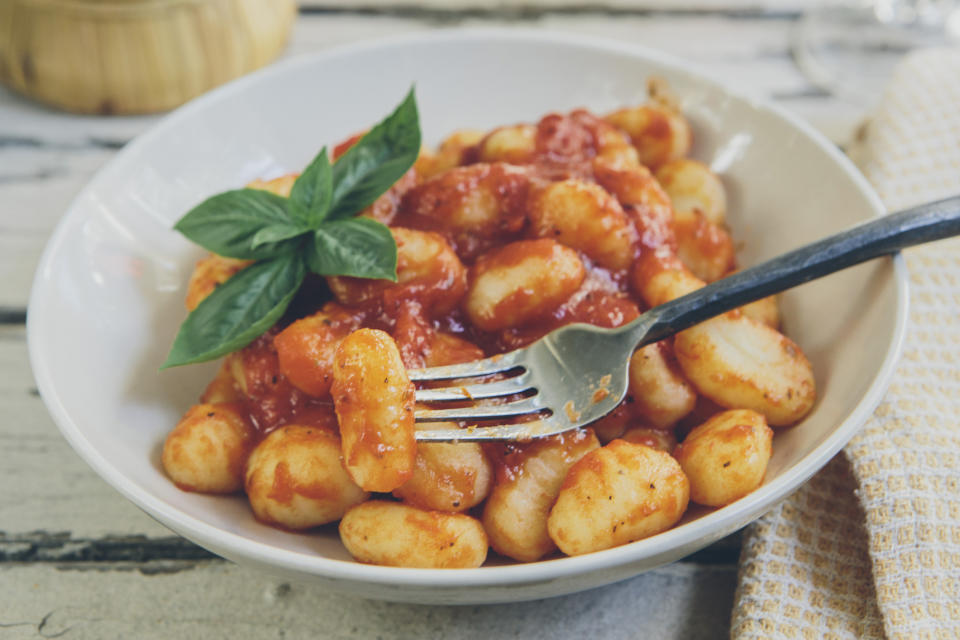 A bowl of gnocchi topped with tomato sauce and garnished with fresh basil, served with a fork