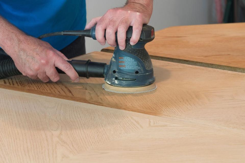 A close up of a person using a tool to refinish a piece of furniture.