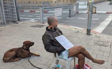 Avichai Brodetz sits with his family's dog Rodney outside the Israeli Defense Ministry offices in Tel Aviv, with a sign reading, 