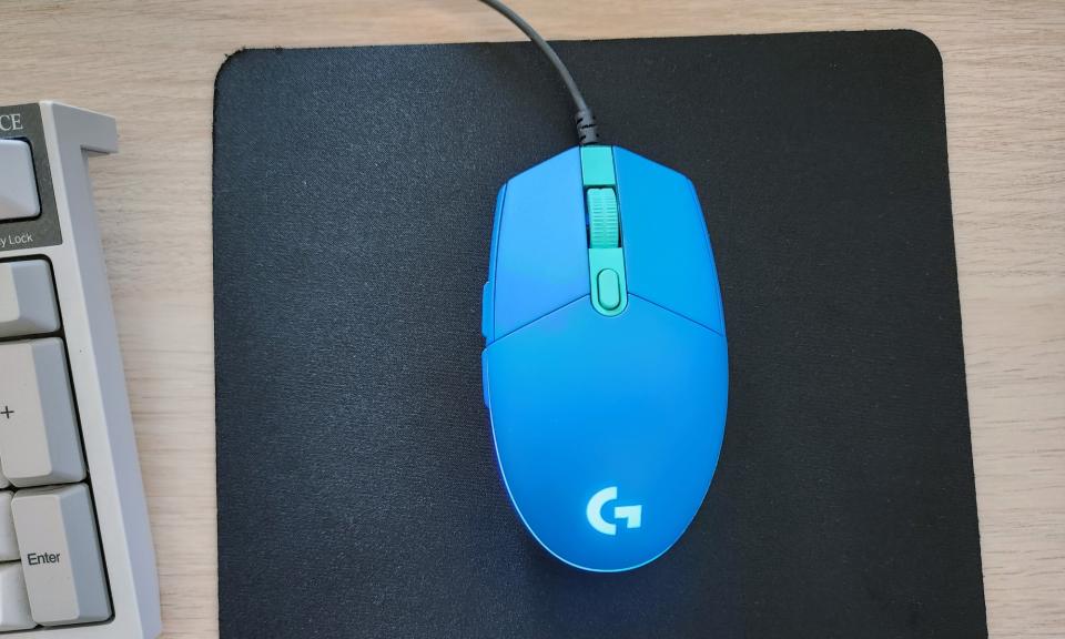 A Blue Logitech G203 Lightsync Gaming Mouse Rested On Top Of A Black Mouse Pad On A Desk.