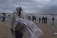 A street hawker covers himself with plastic sheet in rain as he waits for customer to sell cigarettes and chewable tobacco at Juhu beach in Mumbai, India, Thursday, June 30, 2022. India banned some single-use or disposable plastic products Friday as a part of a longer federal plan to phase out the ubiquitous material in the nation of nearly 1.4 billion people. (AP Photo/Rafiq Maqbool)