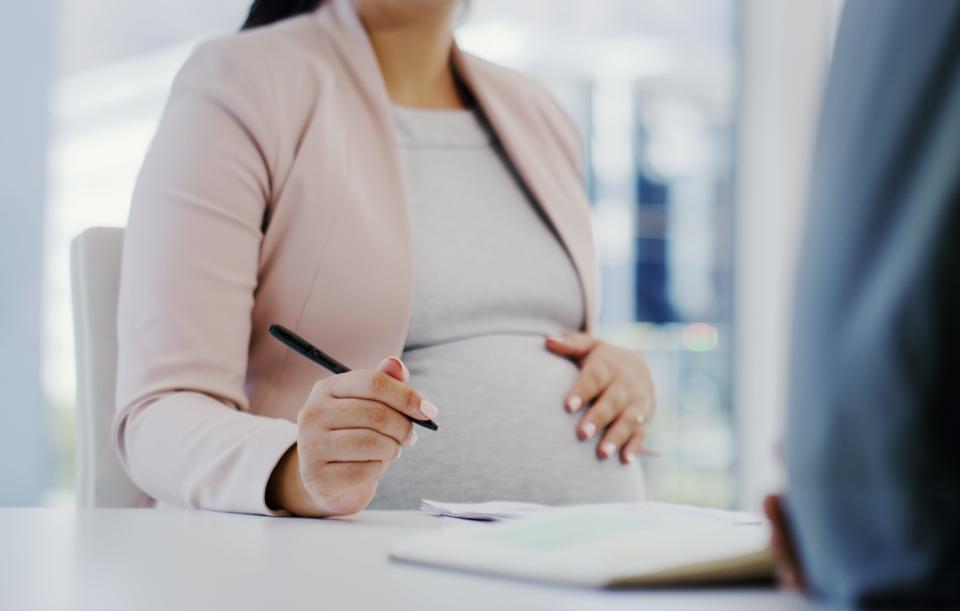 Cropped shot of a woman touching her pregnant belly while sitting in a meeting