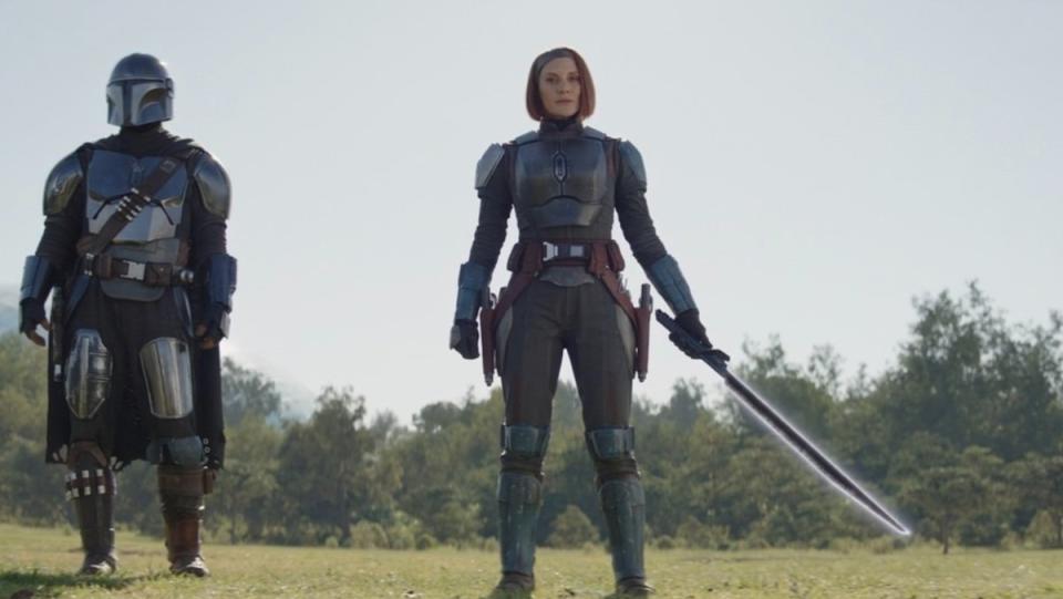 Bo-Katan (center) without her helmet holds the Darksaber by her side as Din Djarin stands next to her on The Mandalorian