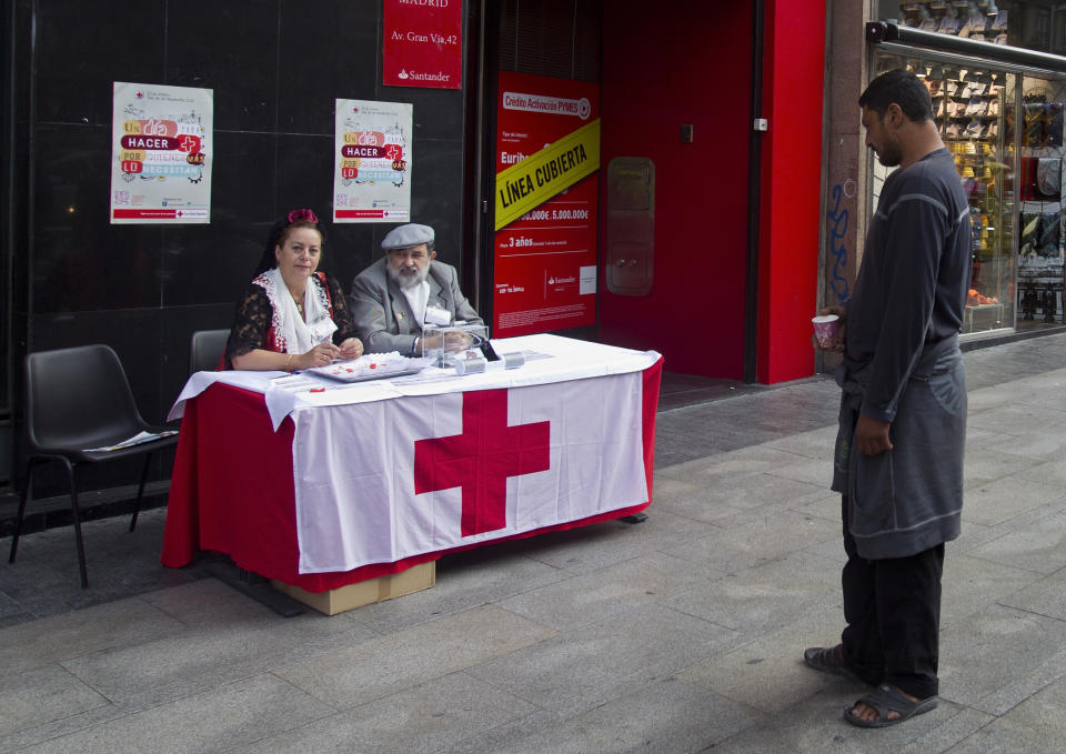 A man begging with a paper cup stands looking at Red Cross volunteers collecting money in the street, in Madrid, Wednesday Oct. 10, 2012. Spain’s Red Cross is launching its first-ever public appeal for donations to help the growing number of Spaniards in need of help because of the economic crisis.Spokesman Miguel Angel Rodriguez said Tuesday the agency is looking to round up some euro 30 million ($38.87 million) over the next two years to help an extra 300,000 people. (AP Photo/Paul White)