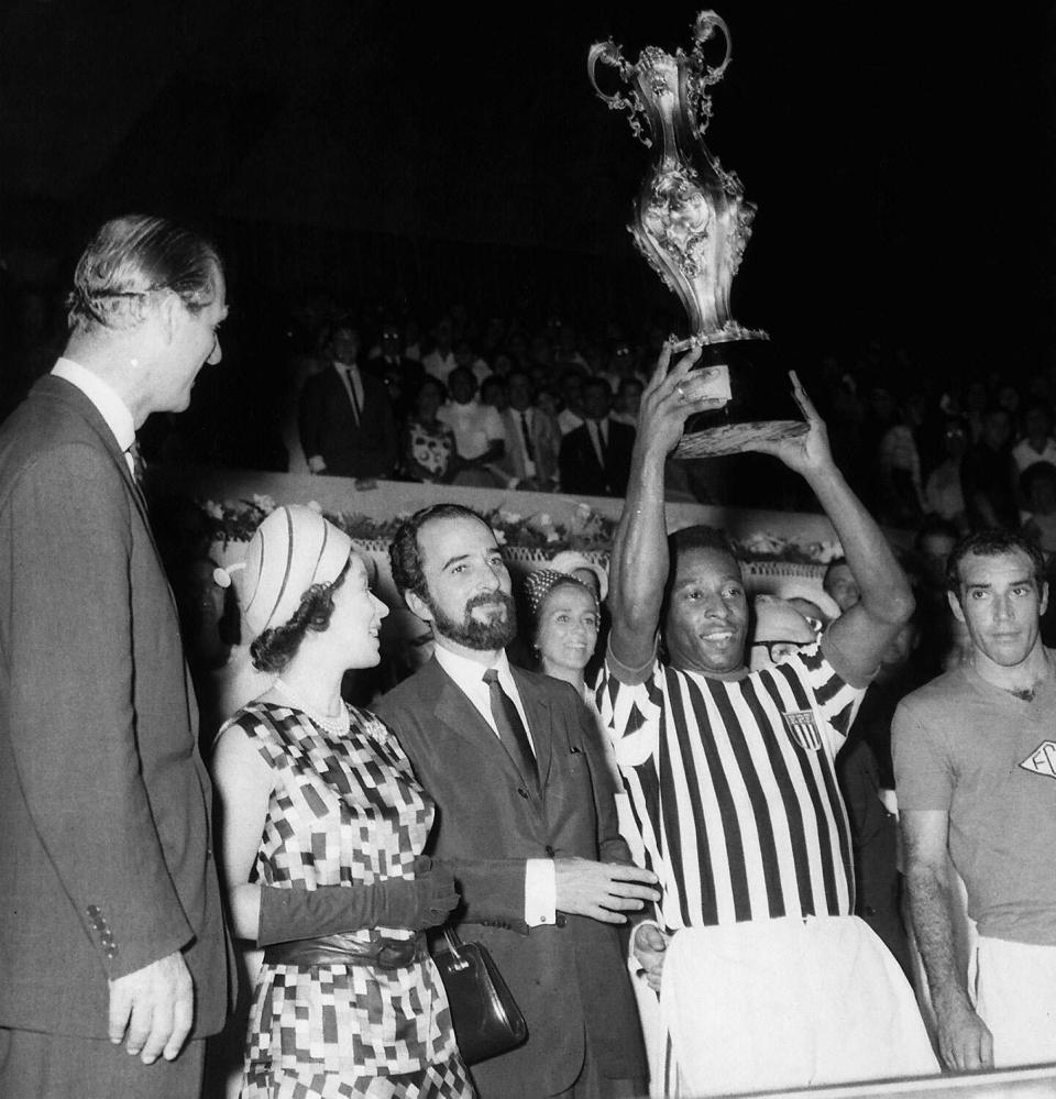 قدمت الملكة إليزابيث الثانية الكأس إلى بيليه بعد أن لعب فريقه سانتوس في ملعب ماراكانا في ريو دي جانيرو بالبرازيل.  الأمير فيليب ، دوق إدنبرة ، ينظر إلى اليسار.  نوفمبر 1968.