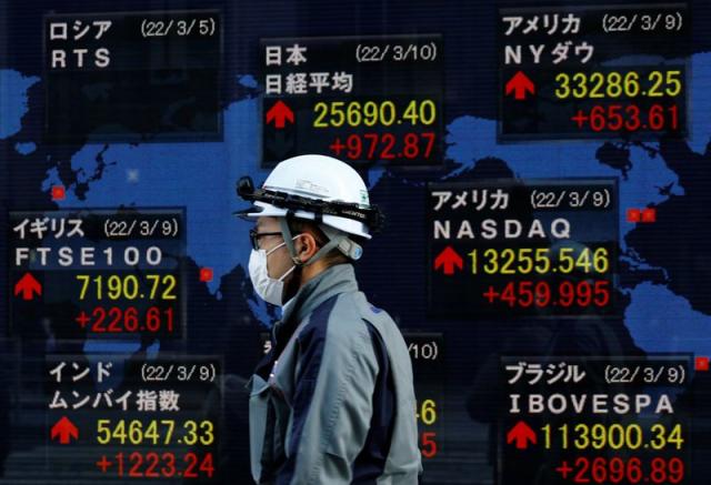 FILE PHOTO:A man wearing a protective mask, amid the coronavirus disease (COVID-19) outbreak, walks past an electronic board displaying various countries' stock indexes including Russian Trading System (RTS) Index which is empty, outside a brokerage in Tokyo