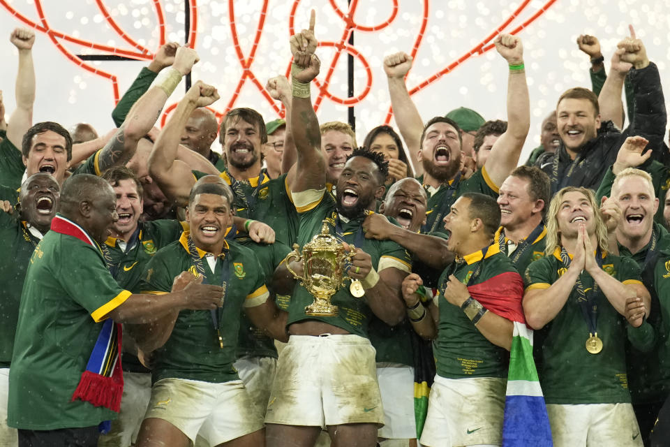 South Africa's Siya Kolisi lifts the trophy as teammates celebrate, as South African President Cyril Ramaphosa, left walks onto the platform during the presentation ceremony after they won the Rugby World Cup final match between New Zealand and South Africa at the Stade de France in Saint-Denis, near Paris Saturday, Oct. 28, 2023. South Africa won the game 12-11. (AP Photo/Christophe Ena)