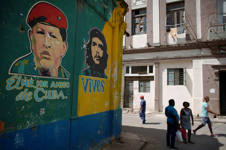 People pass by images depicting Venezuela's late president Hugo Chavez (L), with words that read "The best friend of Cuba", and late revolutionary hero Ernesto "Che" Guevara, in downtown Havana, Cuba, March 13, 2019. REUTERS/Alexandre Meneghini