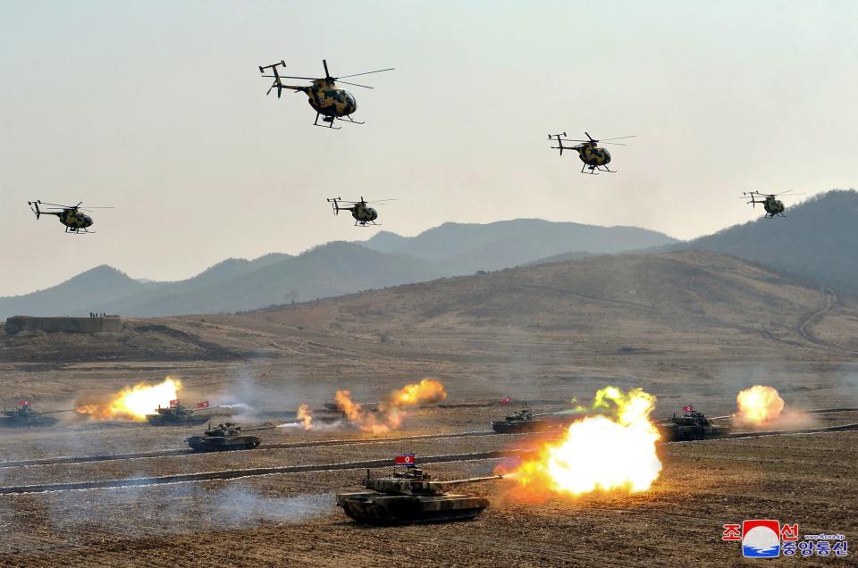 Military helicopters fly above firing tanks during a military demonstration in North Korea.