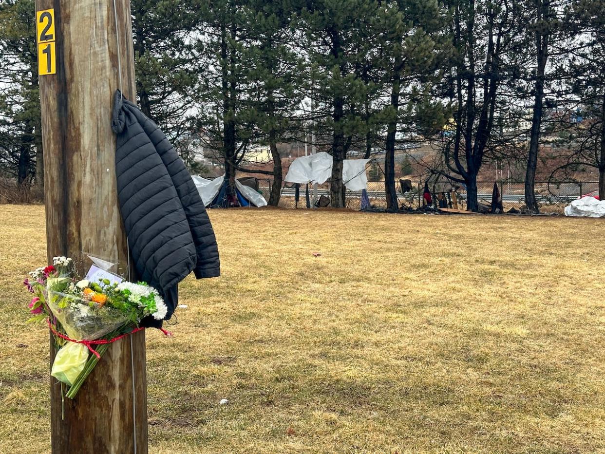 Flowers on a pole near where the bodies of two people were found following a tent encampment fire in Saint John in March.  (Roger Cosman/CBC - image credit)