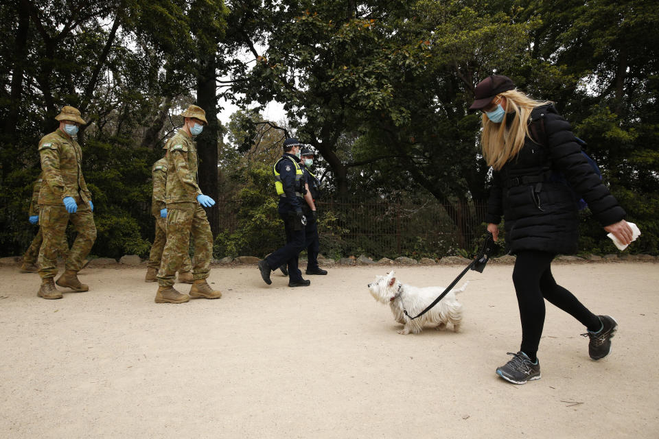 A woman walks her dog as ADF personnel and Victorian police officers pass in a central Melbourne park. Source: AAP