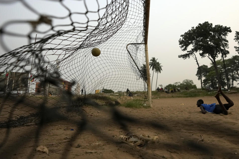 A young man watches the ball after diving while playing football on a dusty field in Abidjan, Ivory Coast, Tuesday, Feb. 6, 2024. (AP Photo/Themba Hadebe)