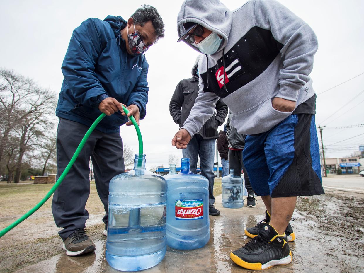 Víctor Hernández y Luis Martínez llenan sus recipientes de agua con una manguera de un grifo en Haden Park en Houston, Texas, el jueves 18 de febrero de 2021 (Brett Coomer/Houston Chronicle/AP)