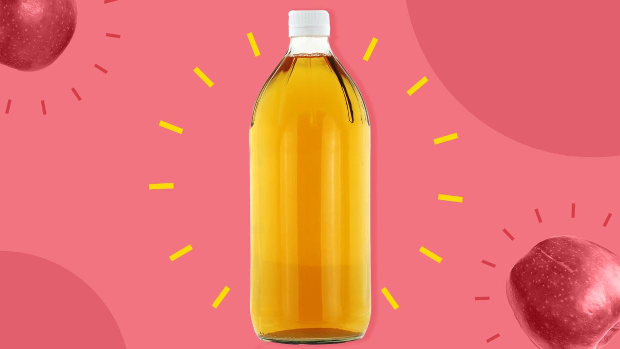 a bottle of apple cider vinegar in front of a pink background dotted with apples