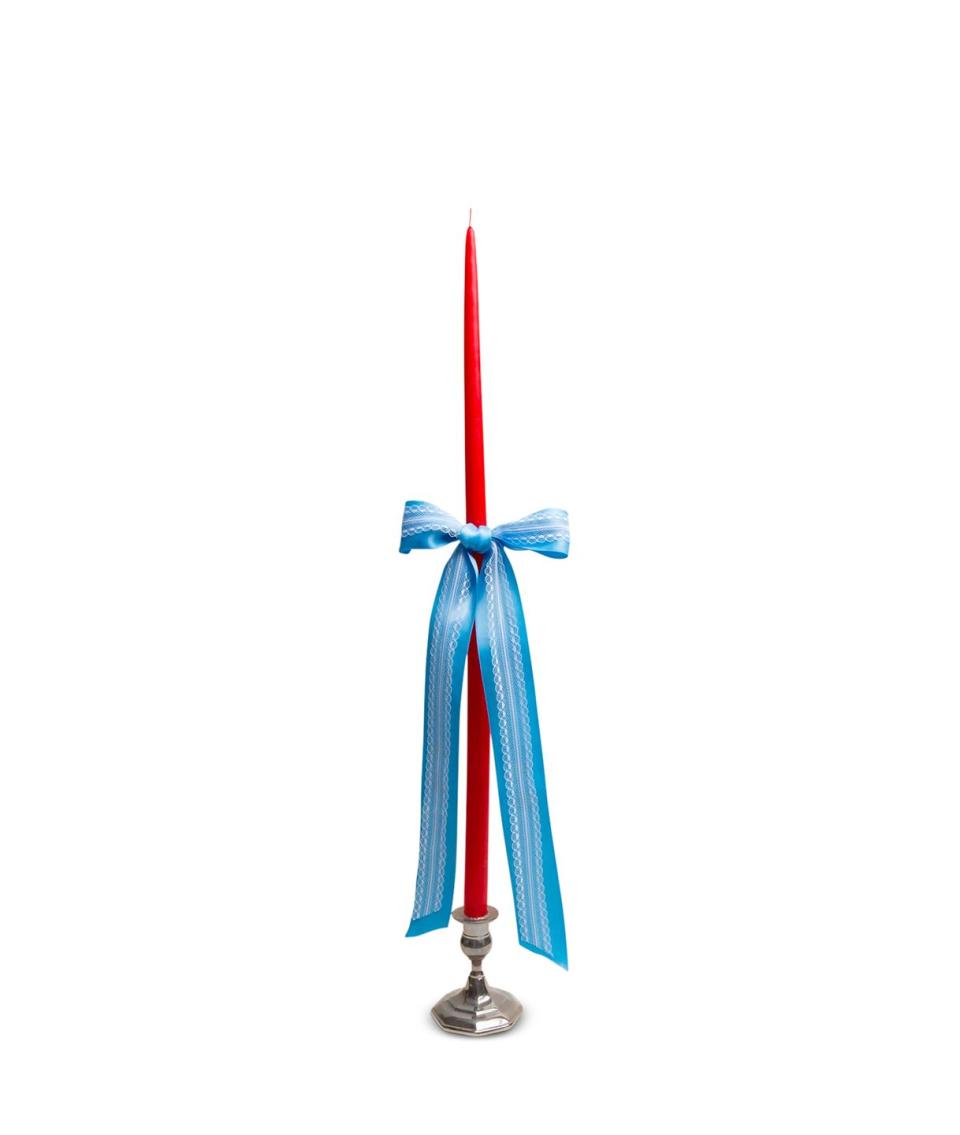 silver candlestick with a long pointy red candle and a blue ribbon