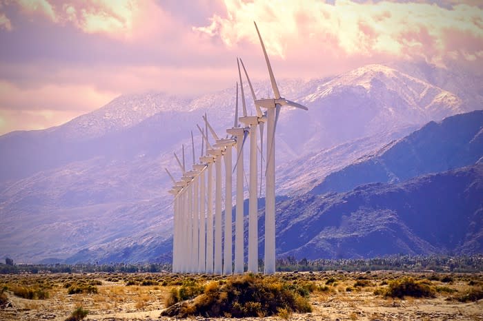 A row of wind turbines with the mountains in the background.