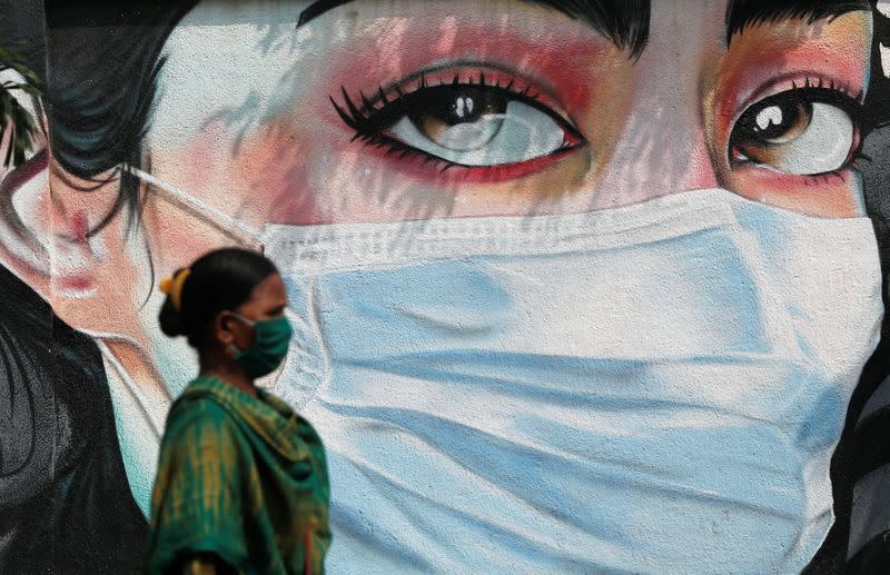 A woman walks past a graffiti of a girl wearing a protective mask amidst the spread of the coronavirus disease (COVID-19) in Mumbai