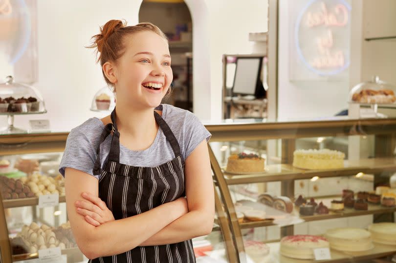 A teenage girl working in a bakery, smiling with her arms folded