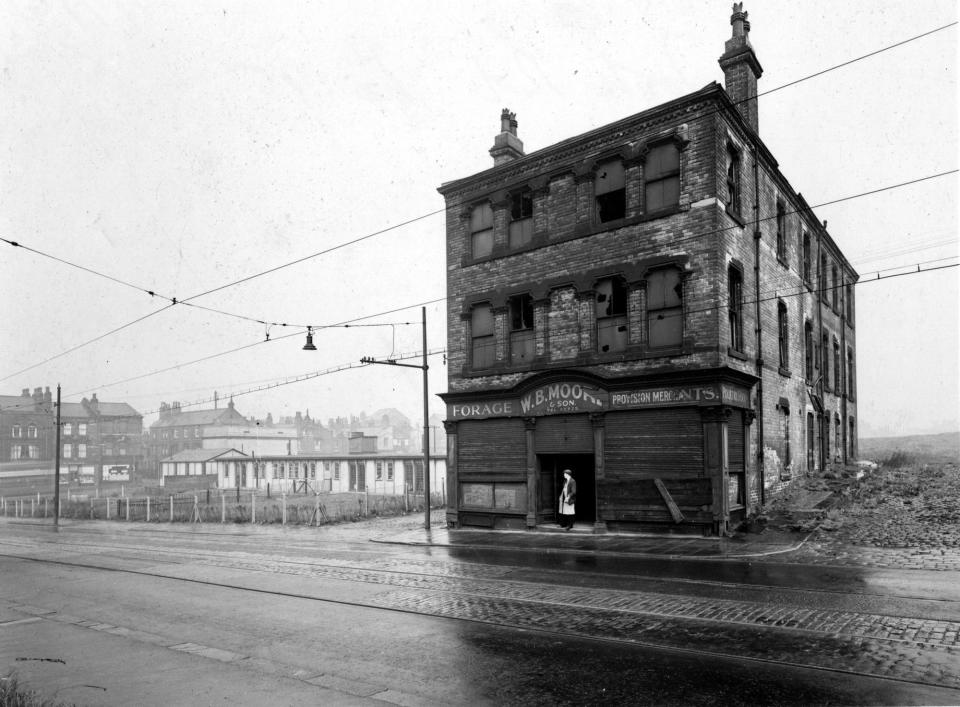 The former premises of W.B. Moore &amp; Son, provision merchants on York Road. The building is derelict, with broken windows and shutters on ground floor windows. A man is standing in the doorway. To the left is a day nursery with some terraced houses behind. Pictured in July 1951.
