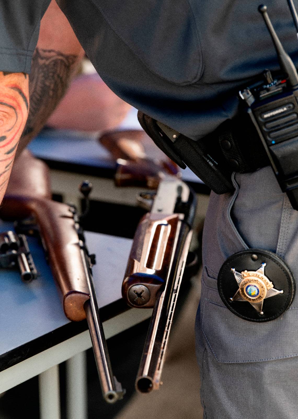 A Durham sheriff’s deputy stands over a shotgun, a rifle and a pistol turned in at a gun buy-back event held by the Durham Sheriff’s Dept., Saturday, Aug. 6, 2022.