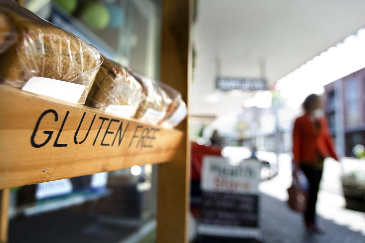 close-up of gluten-free bread shelf at grocery store, woman in distance