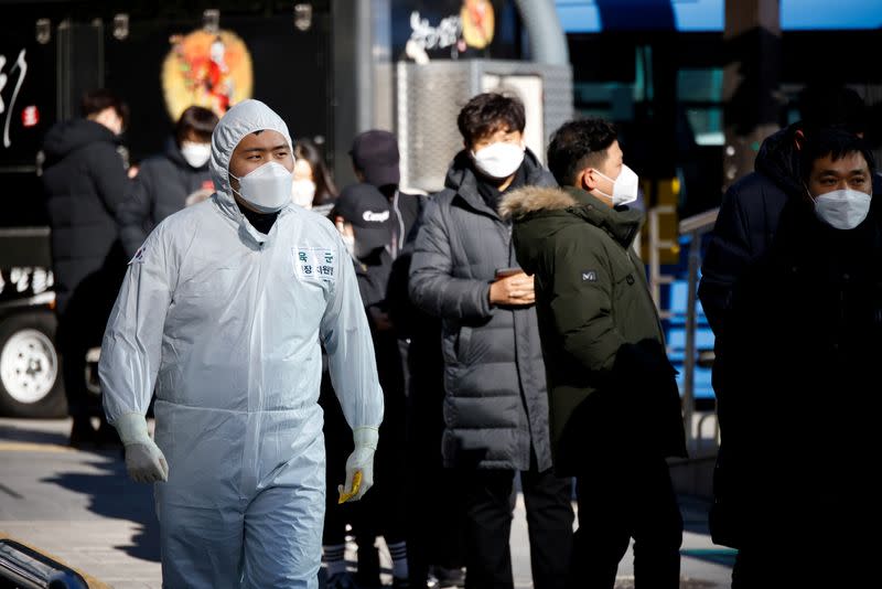 FILE PHOTO: A South Korean soldier wearing a protective suit walks past people who wait in a line to undergo a coronavirus disease (COVID-19) test at a coronavirus testing site which is temporarily set up near a subway station in Seoul