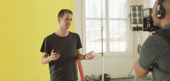 Snap CEO Evan Spiegel stands in front of a yellow background and explains the updated Snapchat design while being filmed by a cameraman