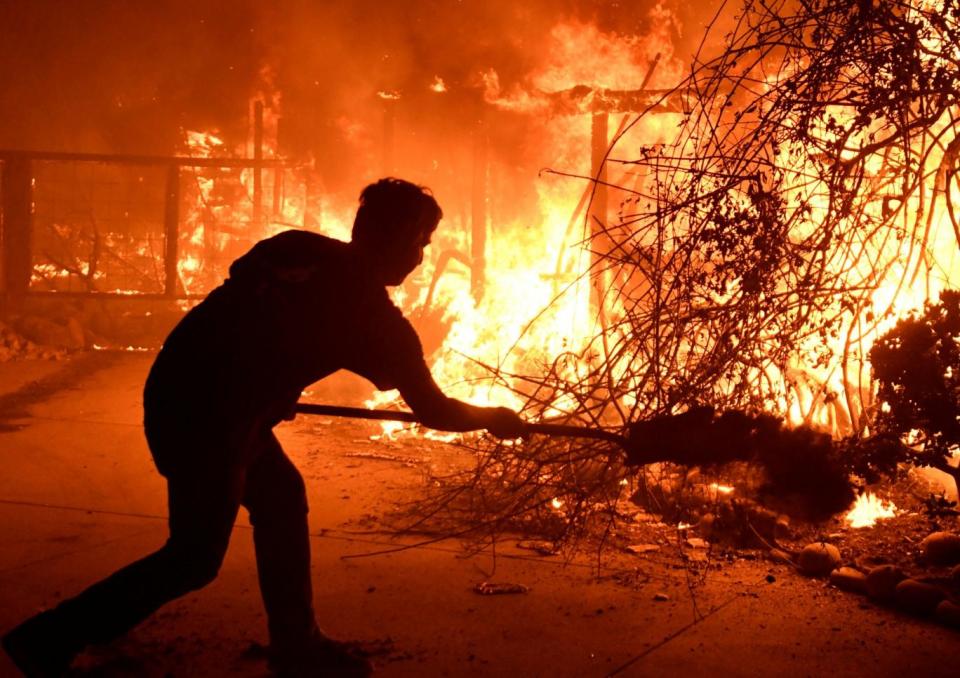 Home owner Will Buckley uses a shovel with dirt to try to stop the flames from from destroying a neighbor's home during the Woolsey Fire in Malibu, California (REUTERS)