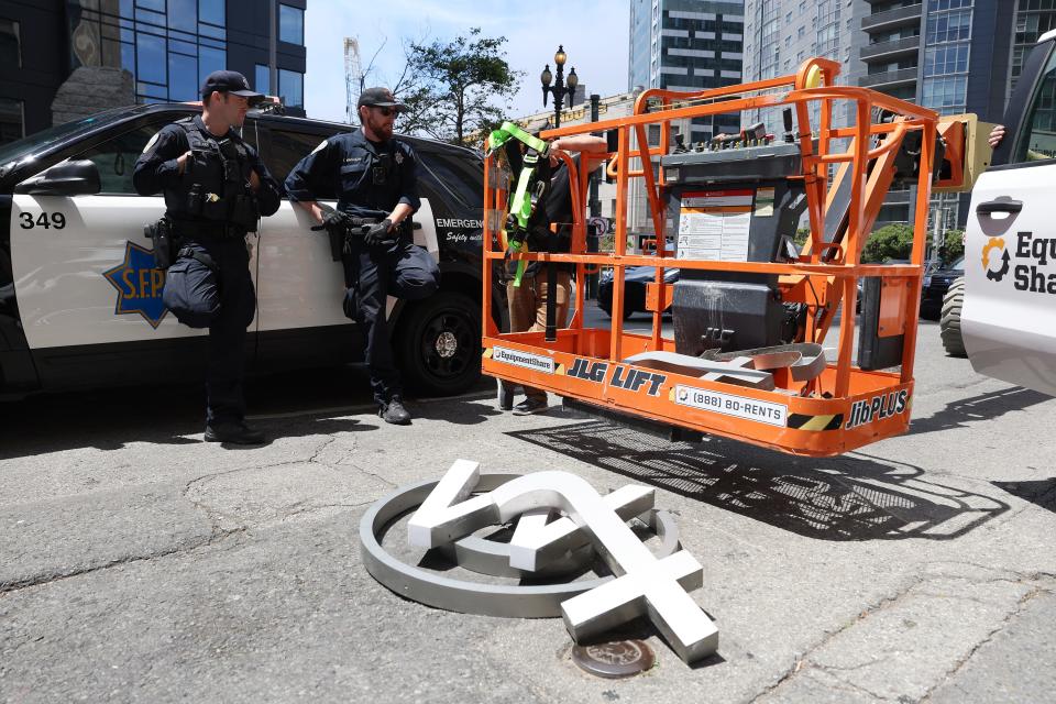 Two police officers leaning against a police car while a worker unclips himself from an orange crane which he was using to take letters from a Twitter sign.