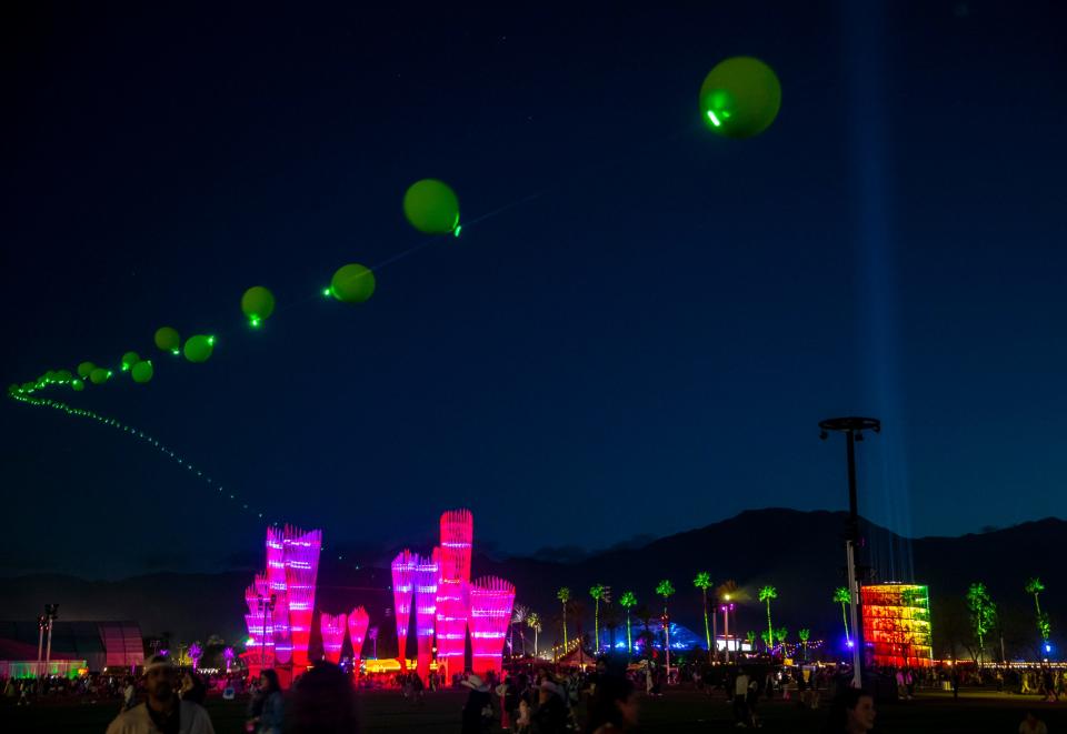 "Balloon Chain" by Robert Bose is seen in the air leading toward "Monarchs: A House in Six Parts" by HANNAH with lights illuminating toward the sky from "Spectra" by NEWSUBSTANCE during the Coachella Valley Music and Arts Festival in Indio, Calif., Saturday.