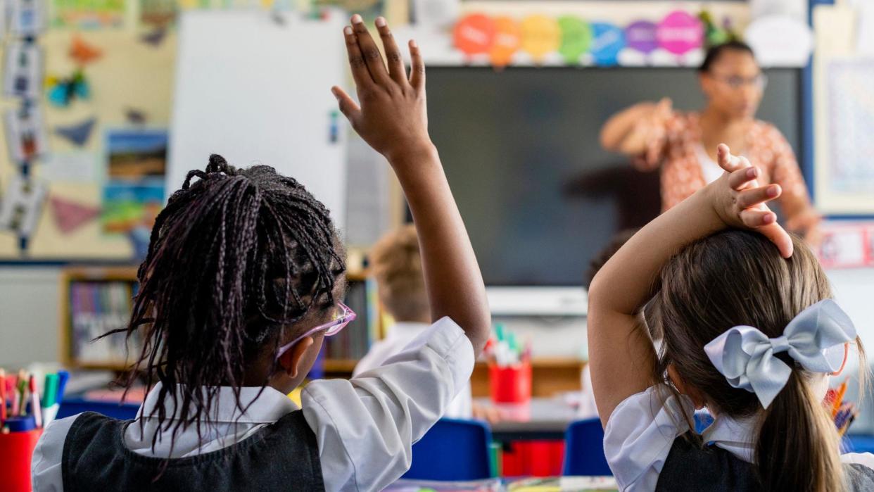 Children putting their hands up in class