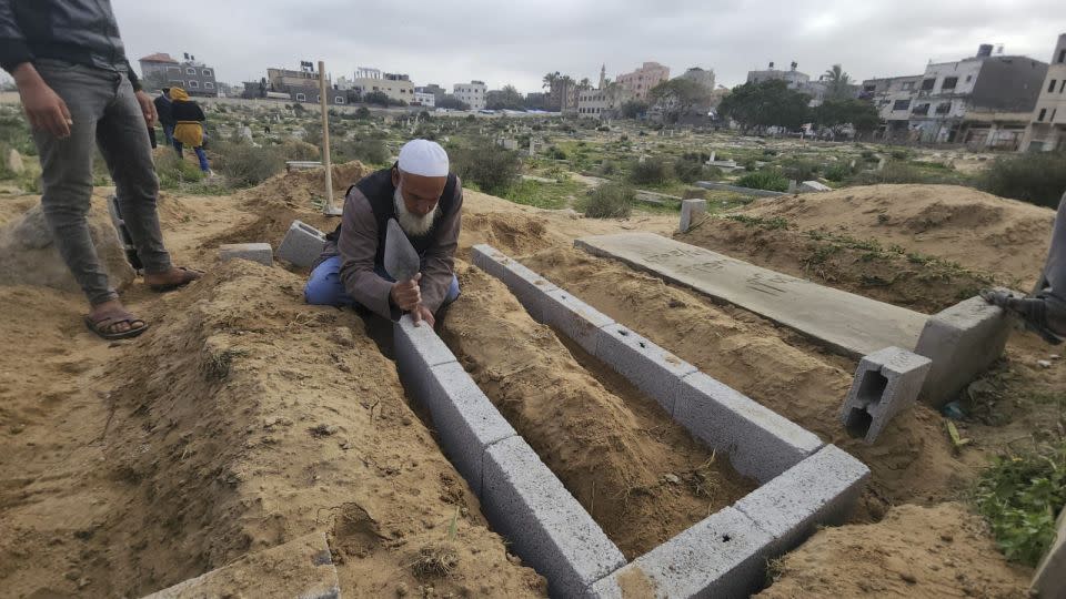 Baraka lays concrete bricks to form the walls of a grave above ground. - Mohammad Al Sawalhi/CNN