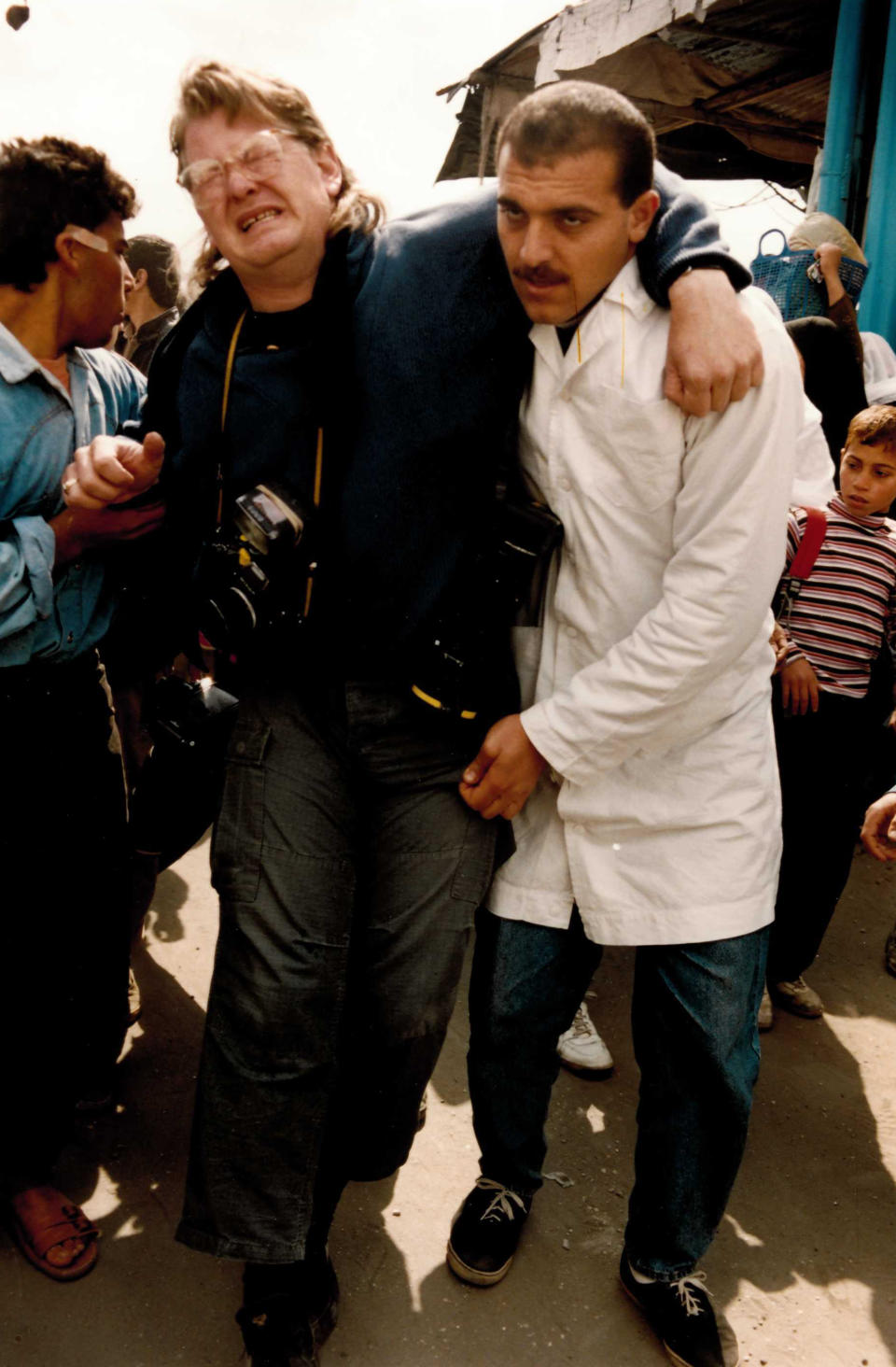 FILE - Associated Press photographer John Gaps III grimaces in pain as he is helped by Palestinian men moments after he was shot in the knee with a plastic bullet while photographing clashes between Palestinian and Israeli soldiers in the occupied Gaza Strip on March 7, 1994. The former award-winning Associated Press photographer, who documented everything from war zones to the NCAA College World Series during his career, was found dead at his home Monday, Oct. 17, 2022, in Des Moines, Iowa, his family confirmed Tuesday. He was 63. (AP Photo/Adel Hana, File)