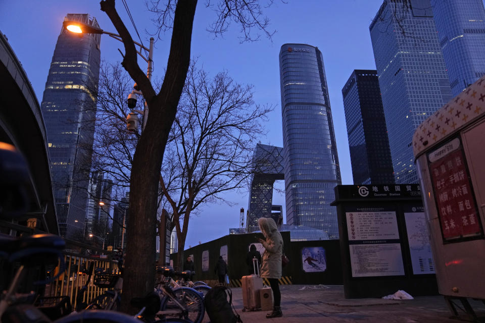 A resident looks at her phone near skyscrapers at the central business district in Beijing, China, Wednesday, Jan. 26, 2022. Richer, more heavily armed and openly confrontational, China has undergone history-making change since the last time it was an Olympic host in 2008. (AP Photo/Ng Han Guan)