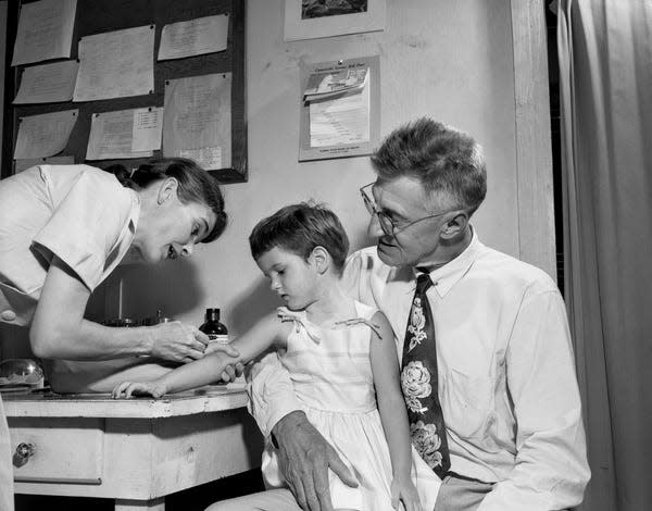 A 3-year-old girl, Dixie Lee Heckel, receives her polio vaccine while sitting on her father's lap in 1957.