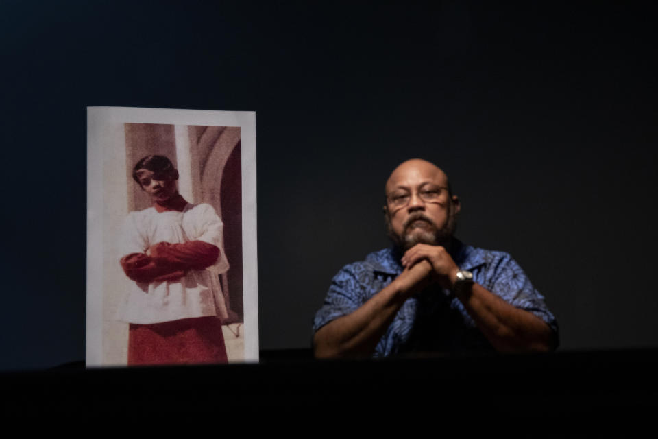 Melvin Duenas, 58, sits beside a photo of himself when he was 11 years old, the age when he says in a lawsuit he was sexual abused by Tomas Camacho and Louis Brouillard, both Catholic priests at the churches where Duenas served as an altar boy, in Hagatna, Guam, Monday, May 13, 2019. "We were taught that when we see a priest we run over there and kneel down," said Duenas. "We looked at them as God himself. I always wanted to be a priest myself. I told my dad shortly after (the abuse happened) and he hit me and said 'don't ever talk about a priest like that.' I tried to commit suicide. I was so upset at God. I tried to numb my thoughts and started drinking. I was a drug addict by the age of 15. A lot of darkness, it just follows me." Camacho and Brouillard are now dead. Brouillard acknowledged abuse allegations before he died. (AP Photo/David Goldman)
