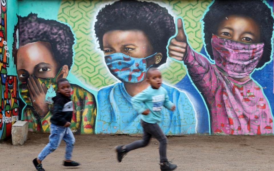 Boys run past a mural by Senzart911, of children wearing face masks, at Soweto's Kliptown, South Africa on October 27, 2021.  - Siphiwe Sibeko/Reuters