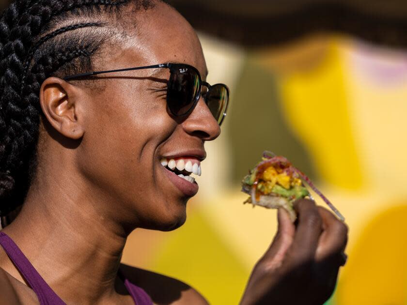 A smiling woman in sunglasses enjoys a slice of avocado toast.